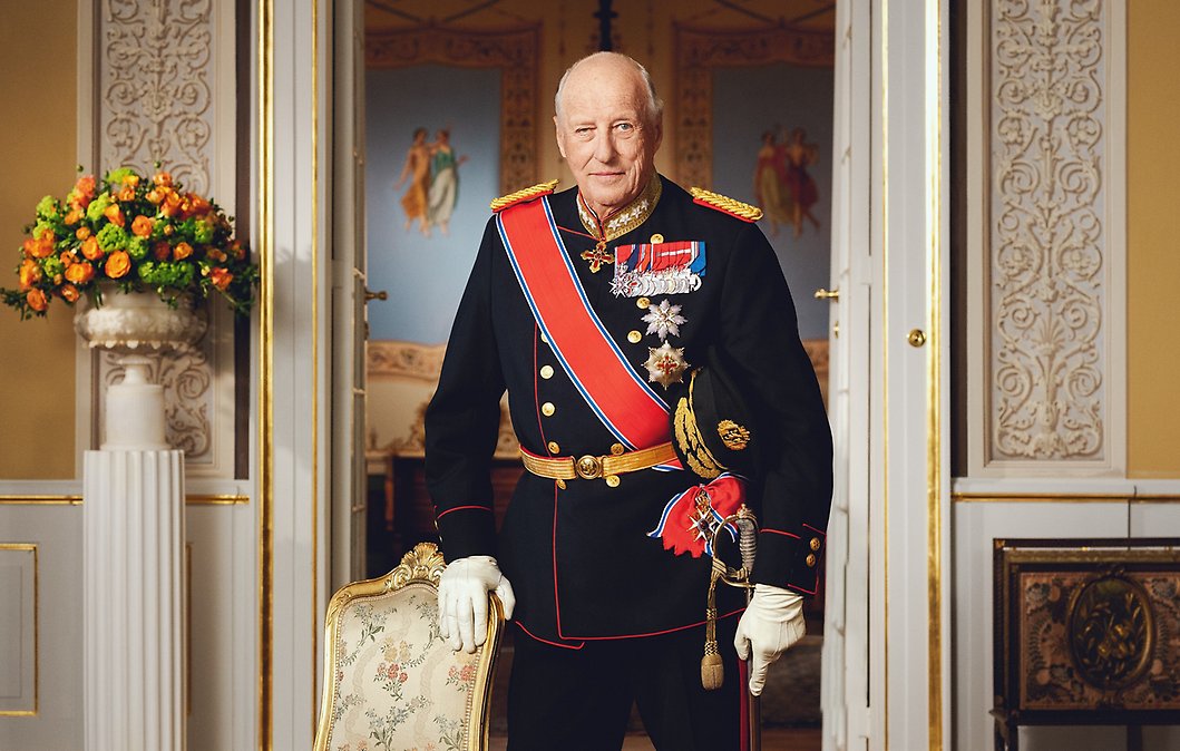 Portrett av Kong Harald stående ved siden av en stol